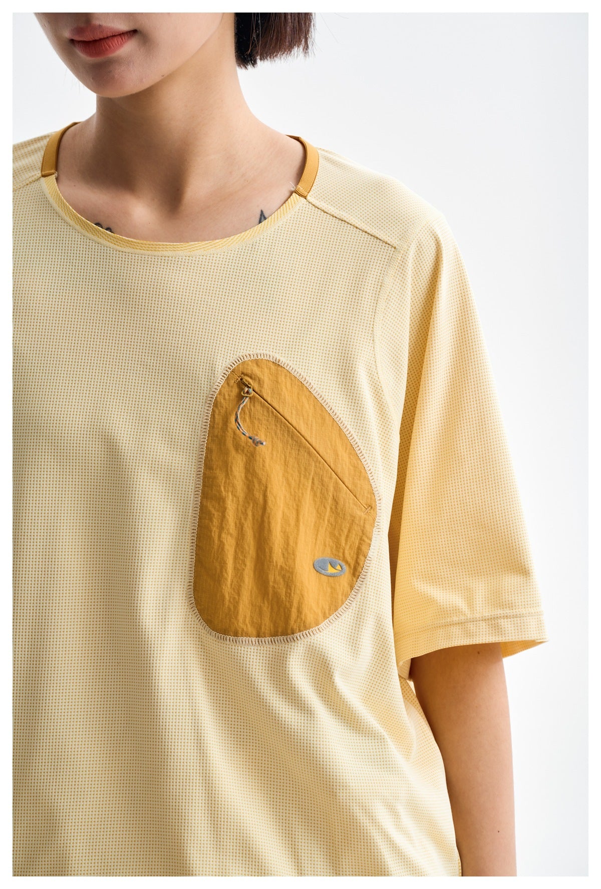Close-up of the pale yellow tee's tiny grid texture, contrast neckline and tan chest pocket with a drawcord.