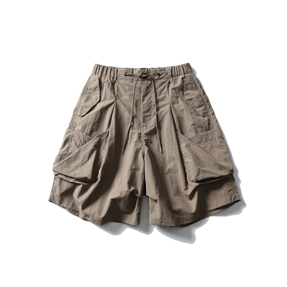 Front view of taupe cargo shorts with an elastic drawstring waist, angled pockets, and large flap side pockets, on white.