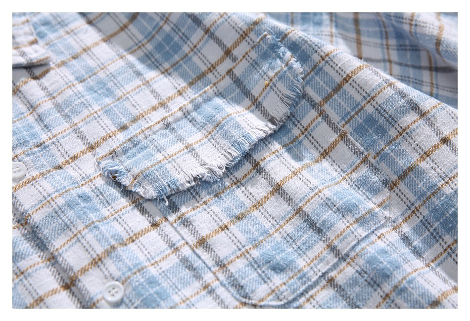 Close-up of a frayed plaid shirt pocket and white buttons in light blue, gray, white, and tan.