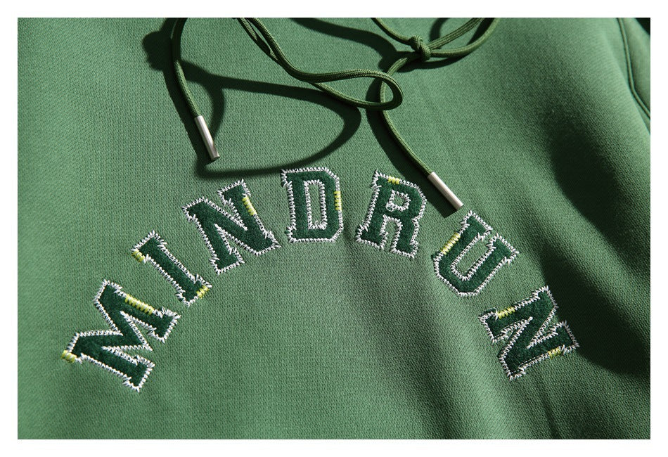 Close-up of arched embroidered lettering and green drawstrings on the hoodie’s chest.