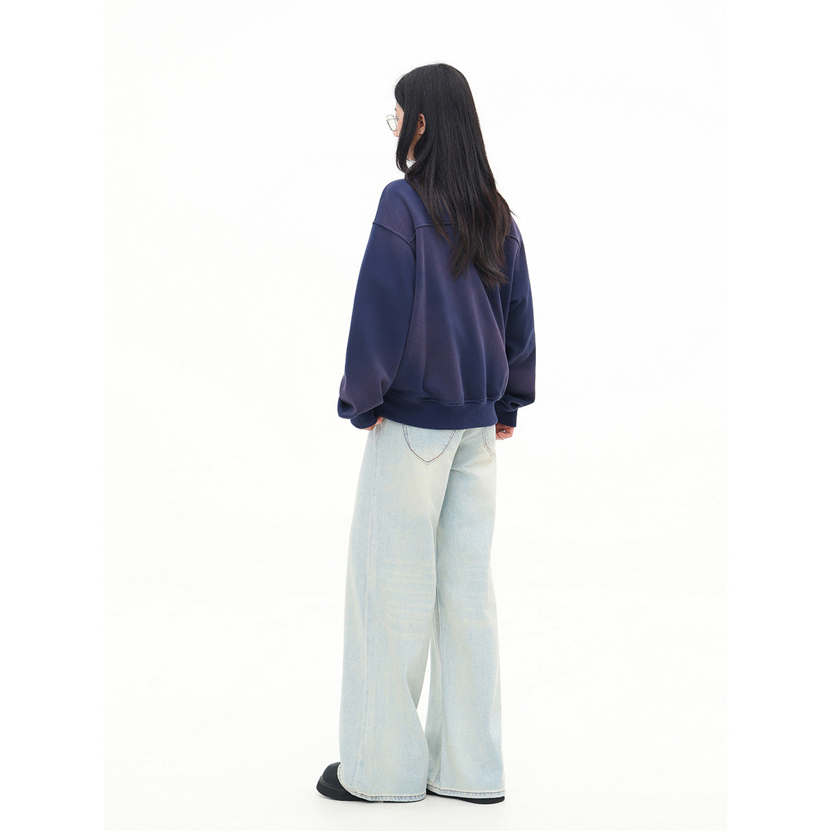 Rear view of a model wearing an oversized navy pullover and pale wide-leg jeans.