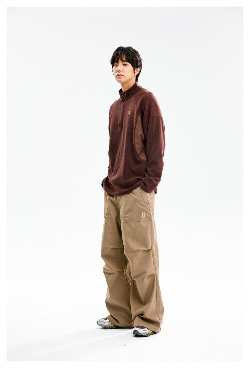 Model wearing a burgundy quarter-zip pullover with brown side panels and loose tan pants, side view.