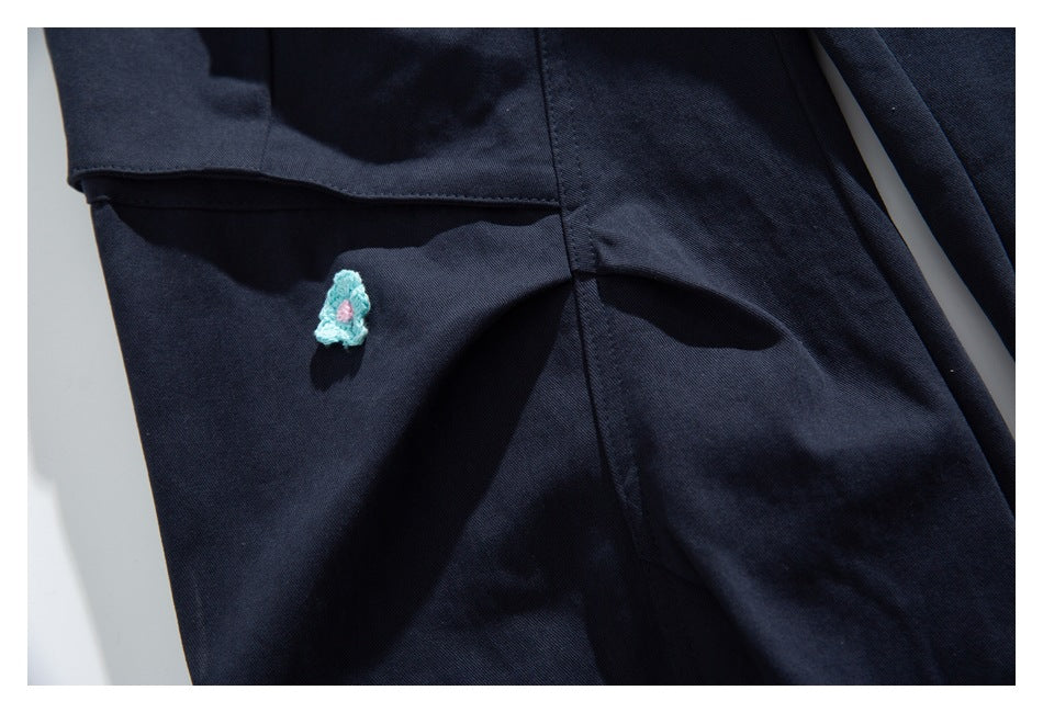 Close-up of a small turquoise and pink stitched motif beside a seam on dark navy fabric.