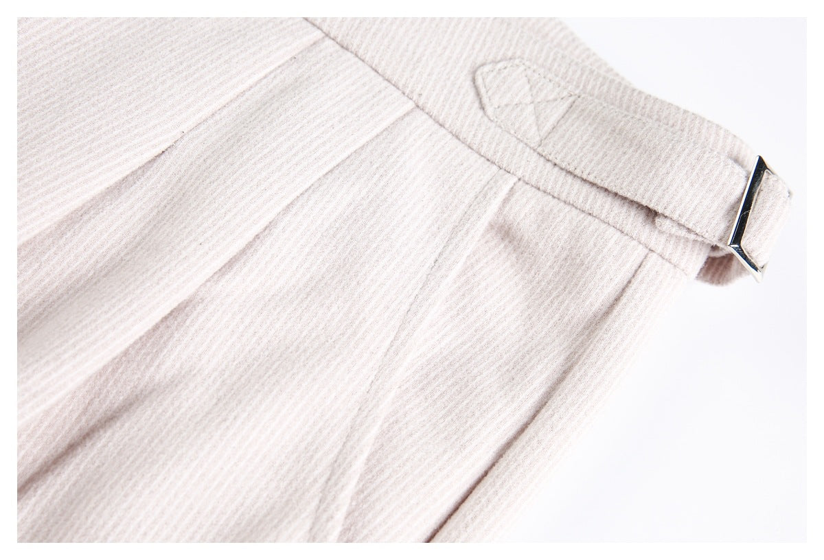 Close-up of pale beige ribbed trousers with a belt loop and rectangular metal buckle.