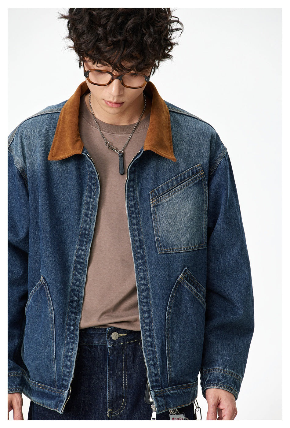 Close view of a dark blue denim jacket showing its brown collar, chest pocket and stitched front details.