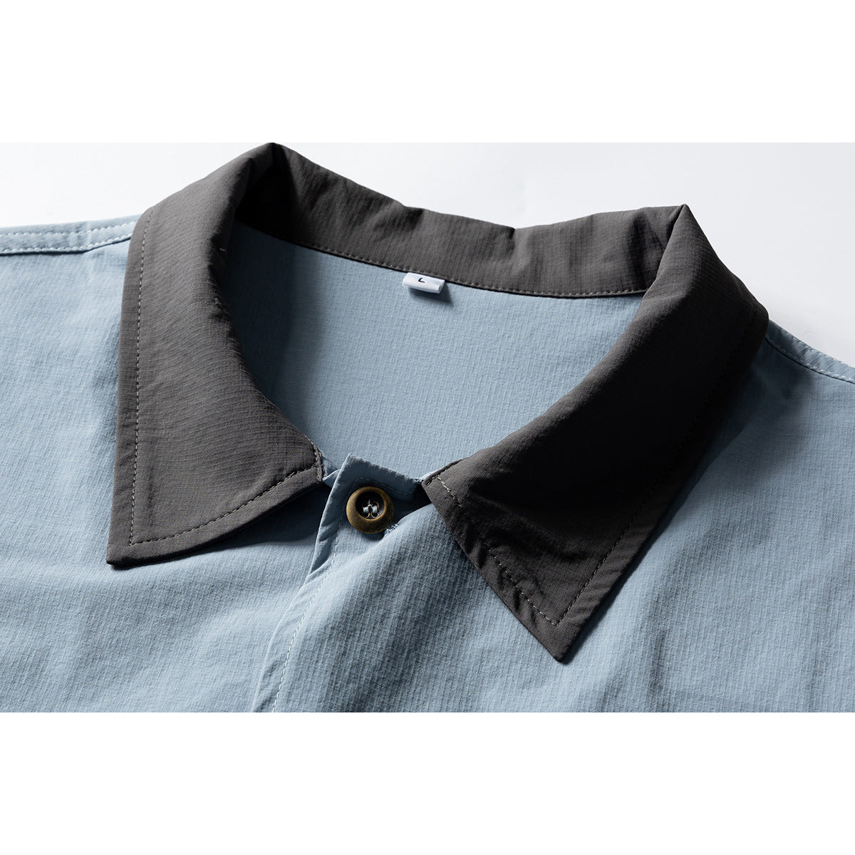 Close-up of a light blue shirt with a contrasting charcoal pointed collar and brown button.