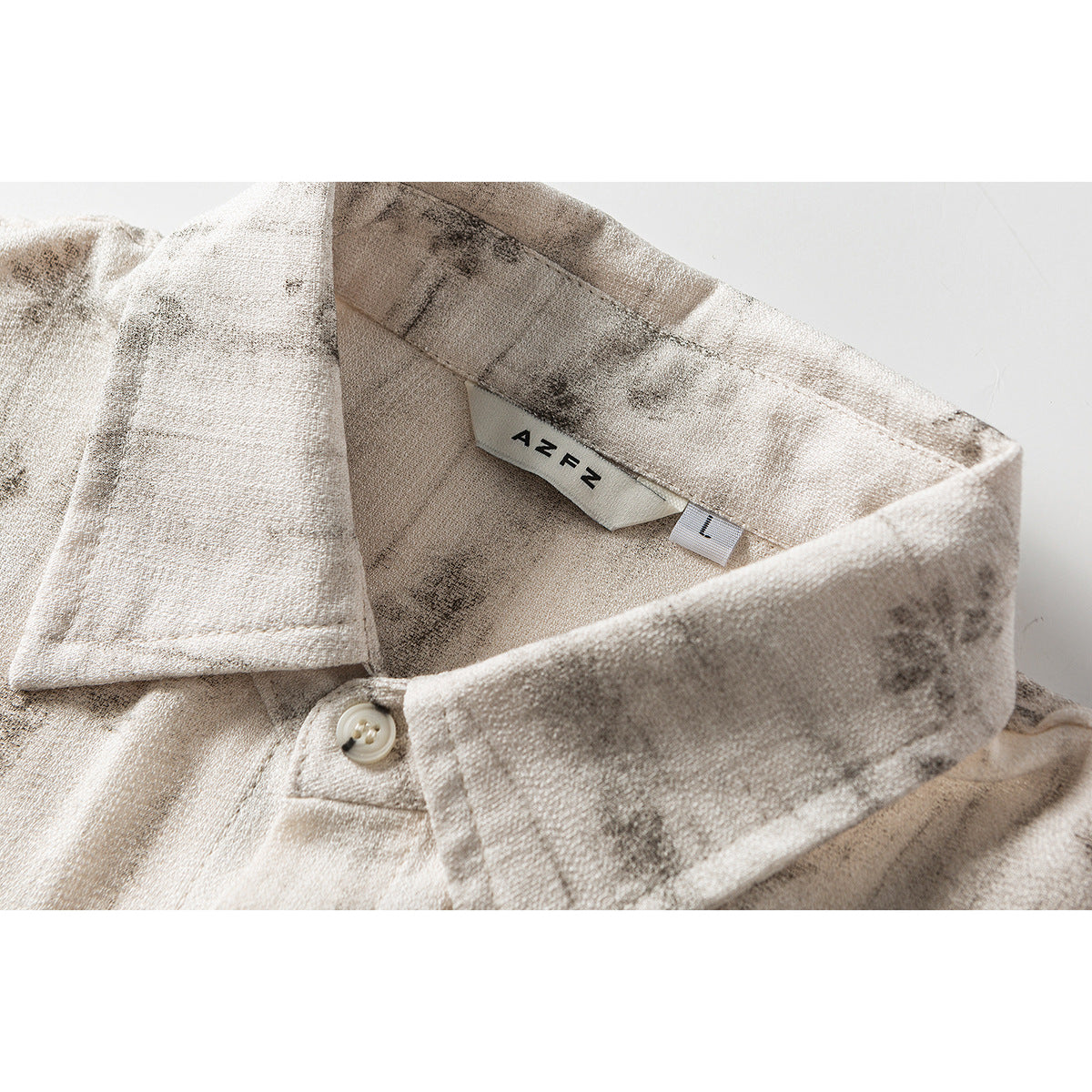 Close-up of a cream-and-gray patterned short-sleeve shirt collar, button, and sewn AZEN label.