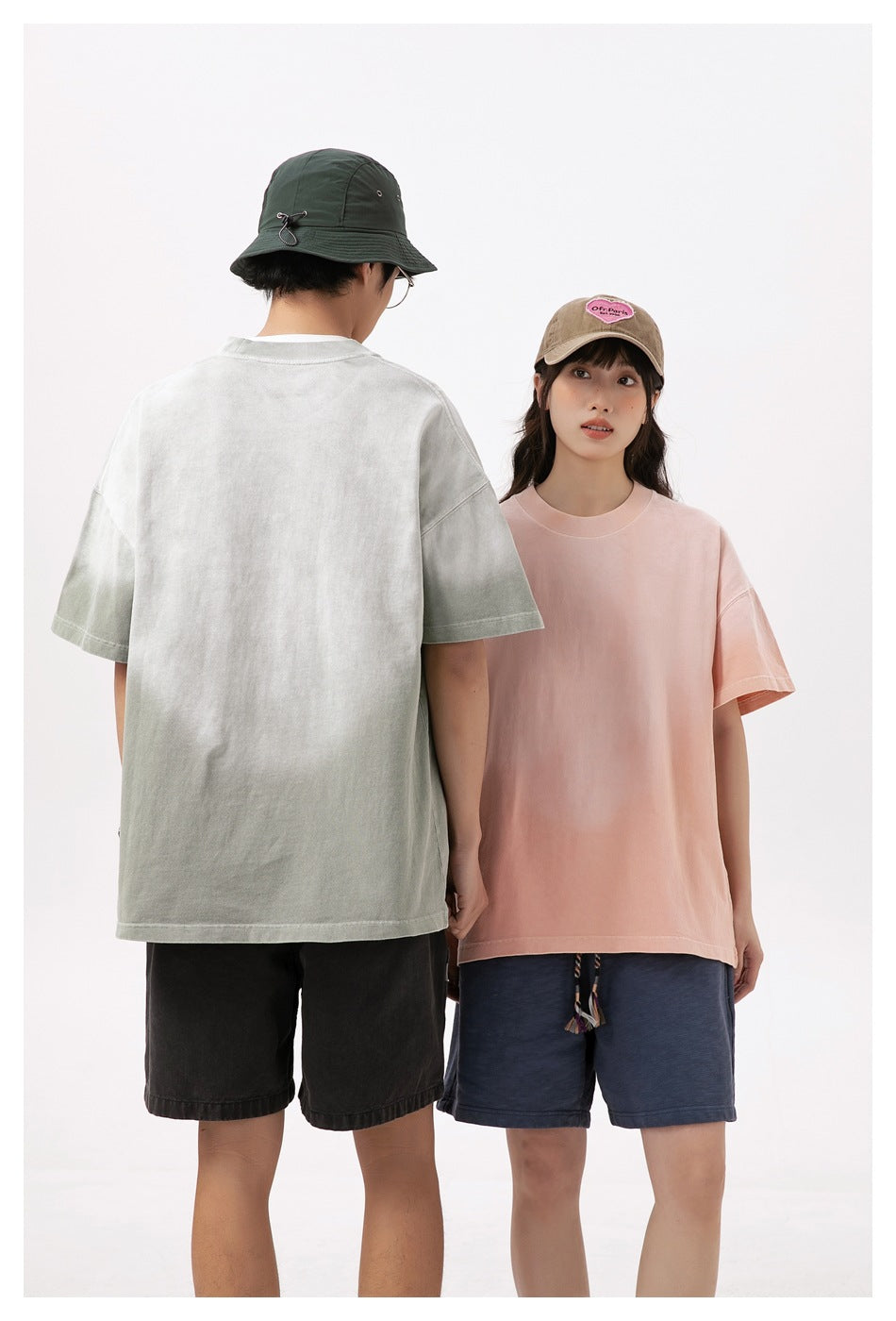 Two models show the T-shirts: a pale sage-gray shirt from the back and a pale pink shirt from the front.
