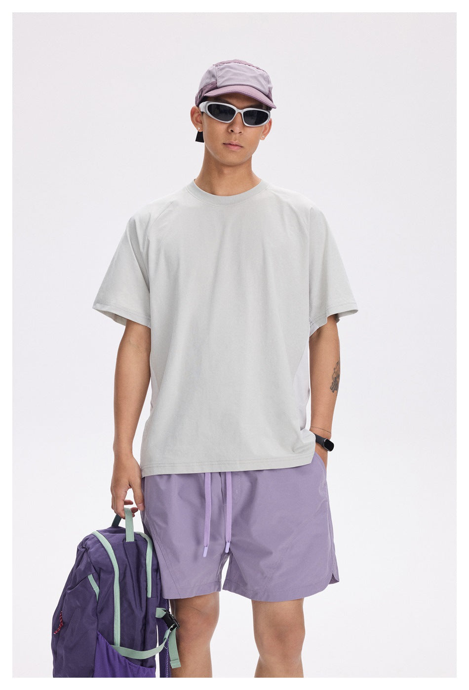 Front view of a model wearing a loose light gray T-shirt with lavender shorts and a cap.