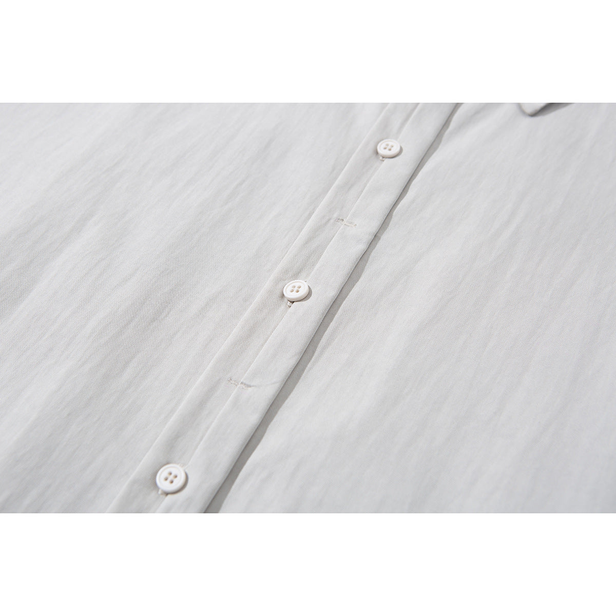 Close-up of the light gray shirt's front placket with three white buttons and visible stitching.