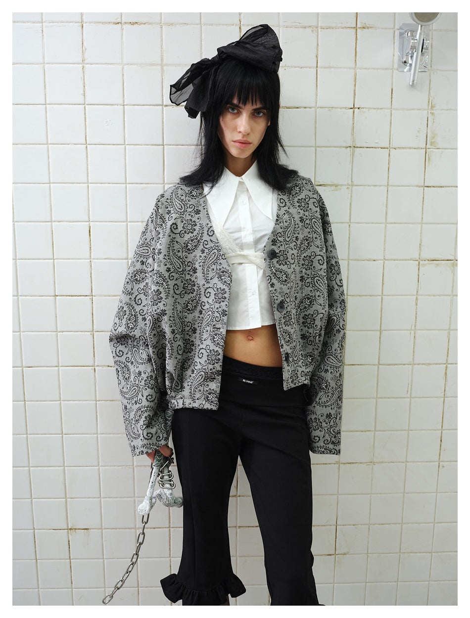 Model wearing a gray, black paisley-patterned button-front jacket over a white cropped shirt and black trousers.