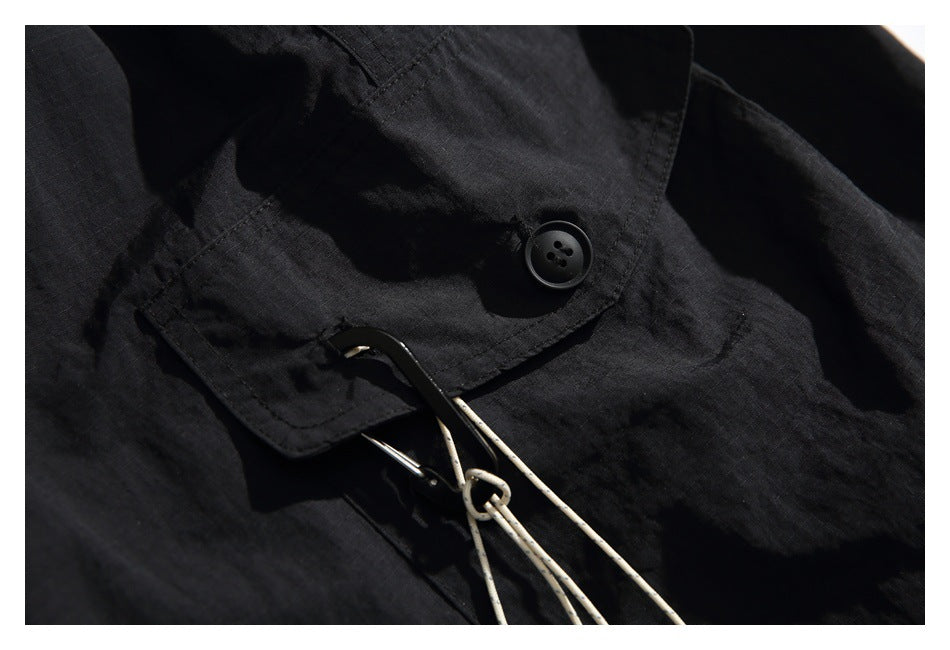 Close-up of a black flap pocket with a button and a metal hook attached to light-colored cords.