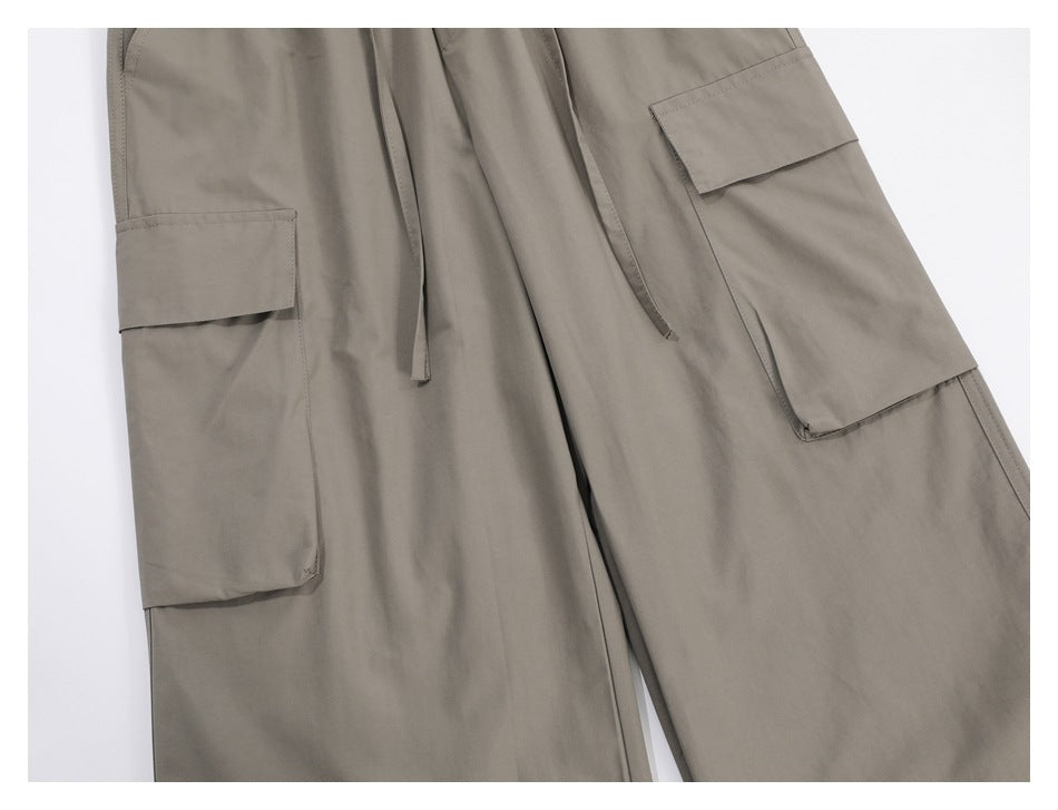 Close-up of taupe cargo trousers showing large flap pockets and dangling waist drawstrings.