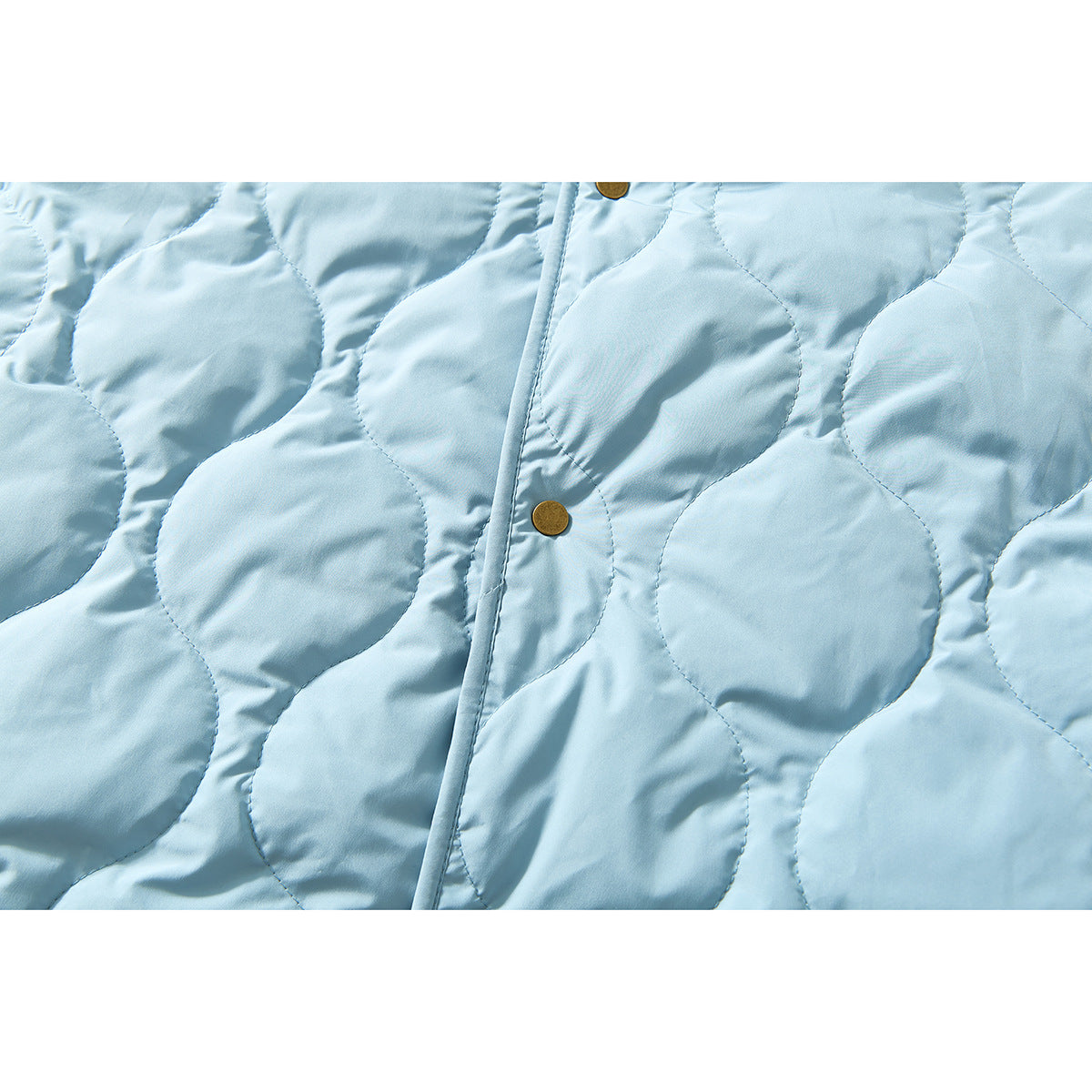 Close-up of the pale blue jacket's circular quilting, front placket, and brass snap buttons.