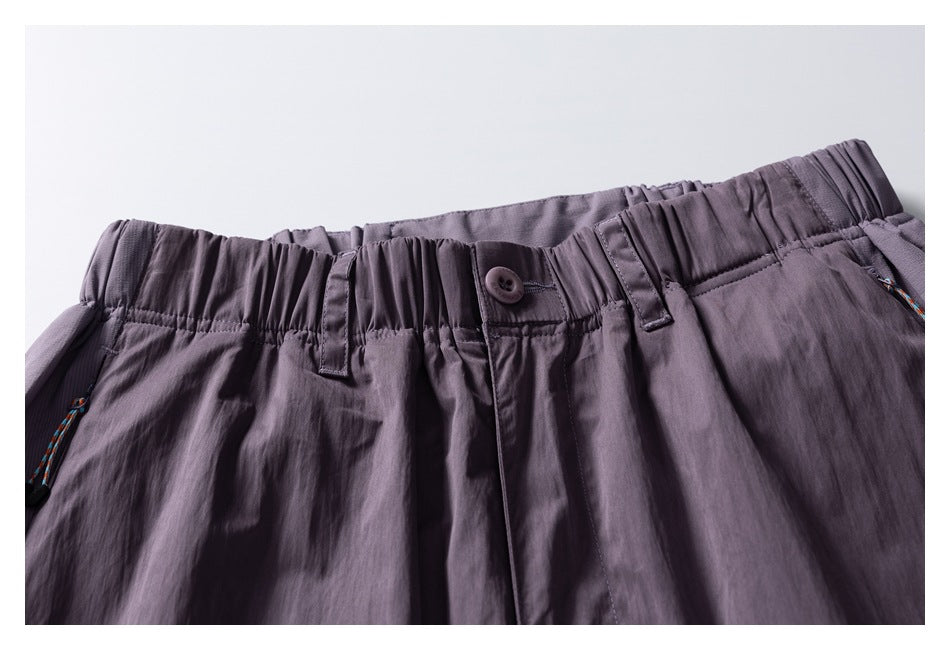 Close-up of mauve-gray pants showing the gathered elastic waistband, button, belt loops, and drawcord ends.
