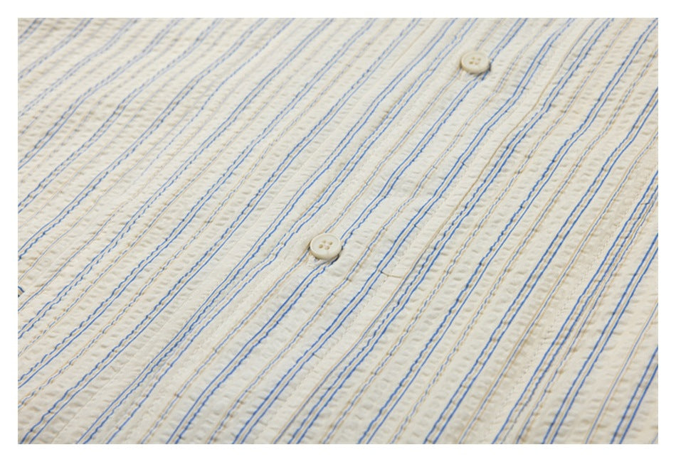 Close-up of cream shirt fabric with fine blue and tan stripes and two cream buttons.