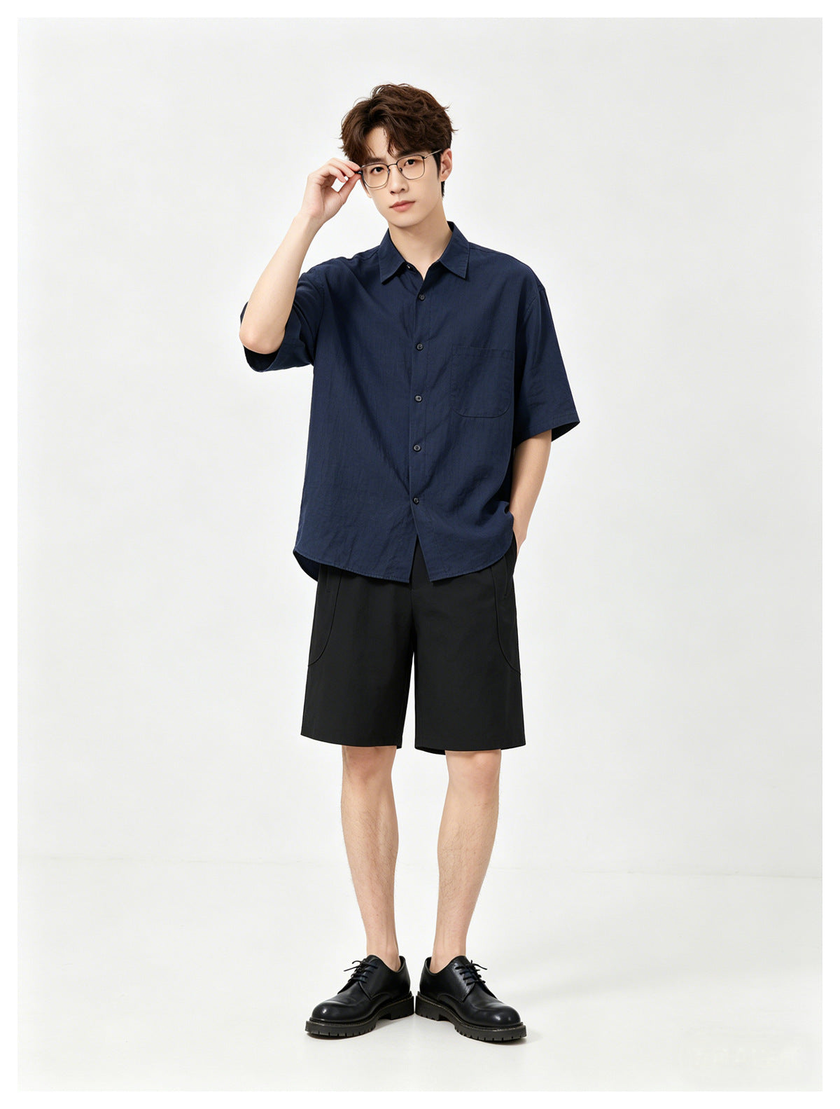 Model wearing black knee-length shorts with a navy short-sleeve shirt and black lace-up shoes, full-length view