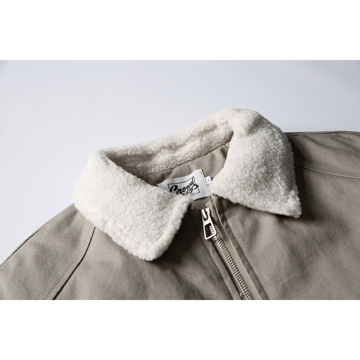 Close-up of a taupe-gray jacket with a plush cream collar, front zipper, and visible neck label.