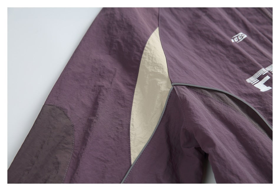 Close-up of the plum jacket's cream color-block panel, dark piping, and sleeve seam.
