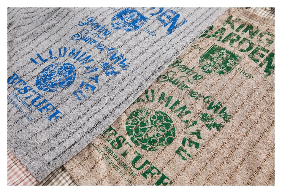 Close-up of gray and beige textured shirt fabric with large blue and green printed English lettering and crest-like graphics.