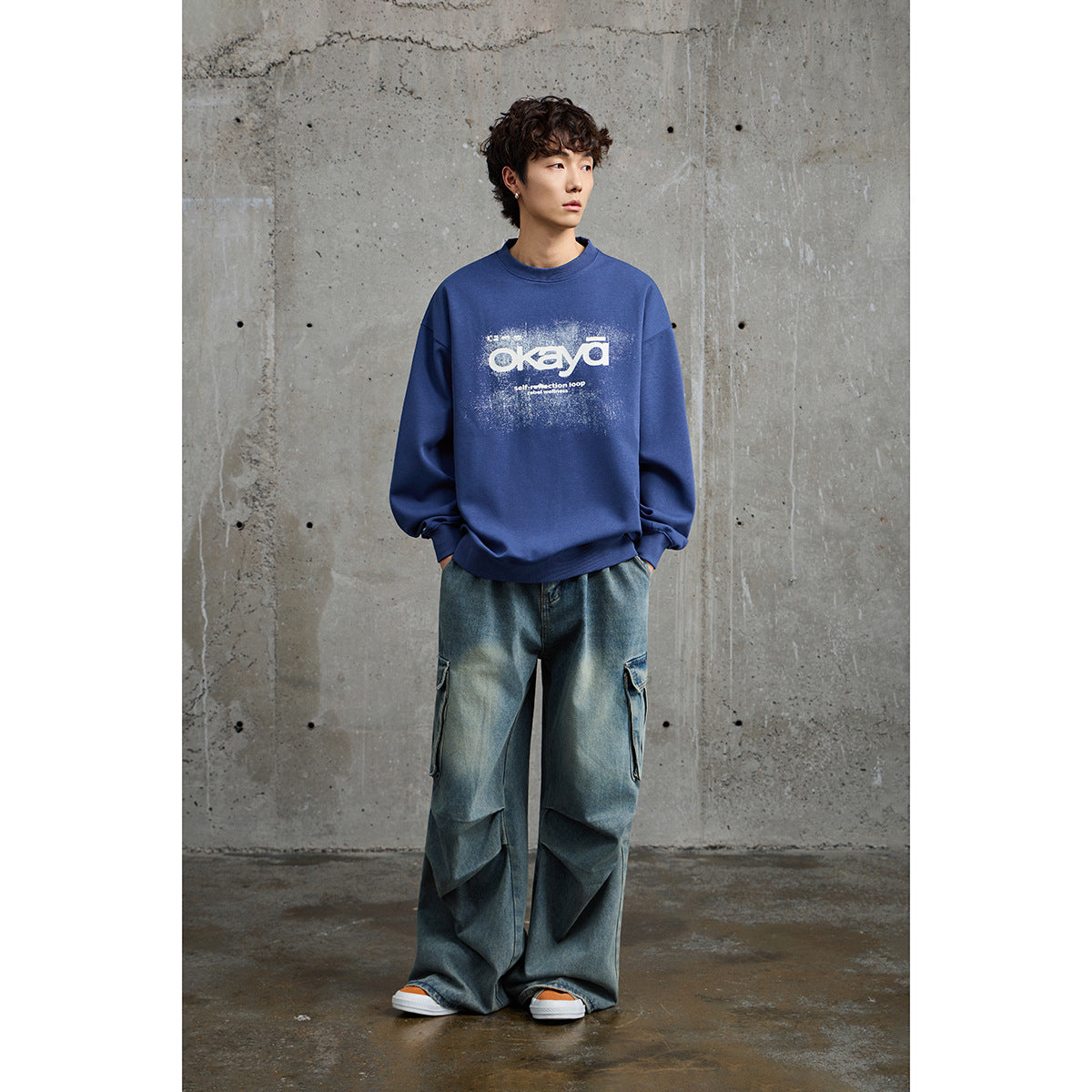 Full-length model wearing a blue oversized crewneck sweatshirt with a white distressed front graphic.