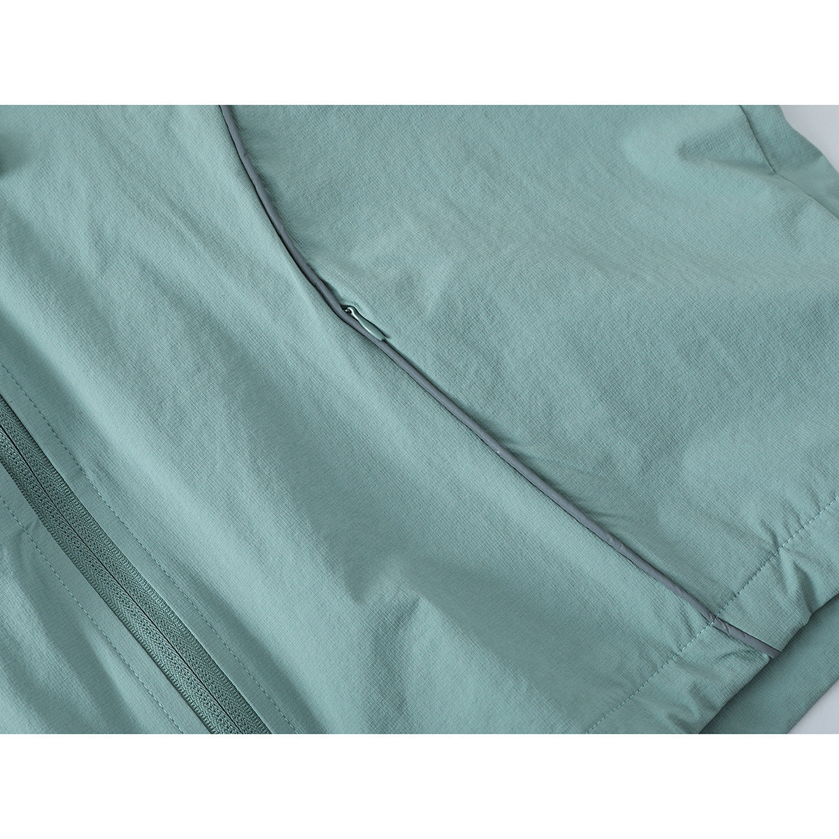 Close-up of pale aqua jacket fabric, zipper, curved piping and a small zippered pocket.