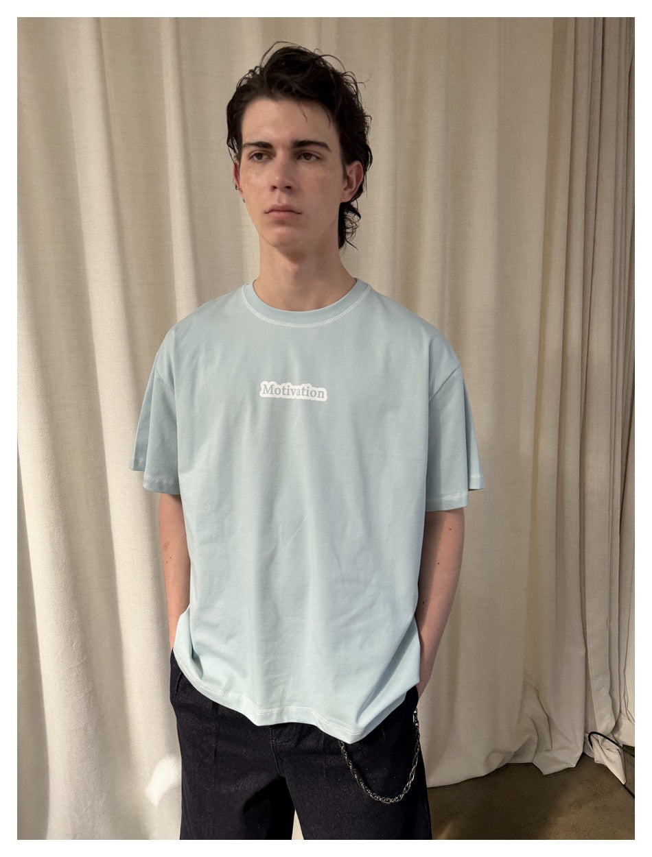 Closer front view of a model wearing a pale blue T-shirt with a small white “Motivation” chest print.