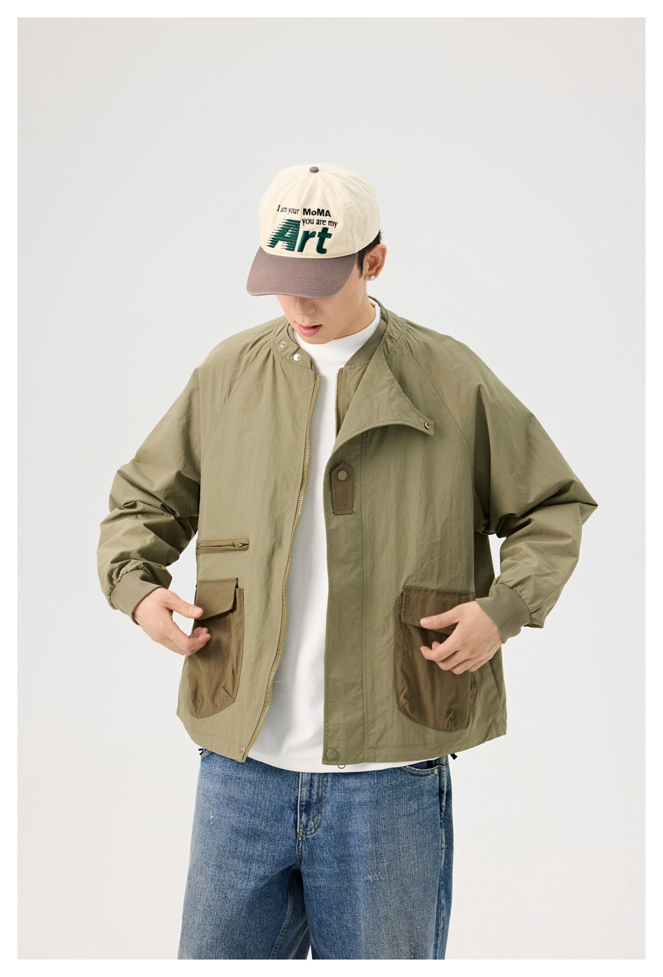 Model wearing an open olive jacket with brown utility pockets, ribbed cuffs and snap collar, over a white shirt and jeans.