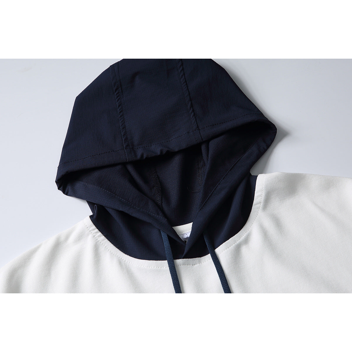 Close-up of a white short-sleeve hoodie with a dark navy hood and matching drawstrings.