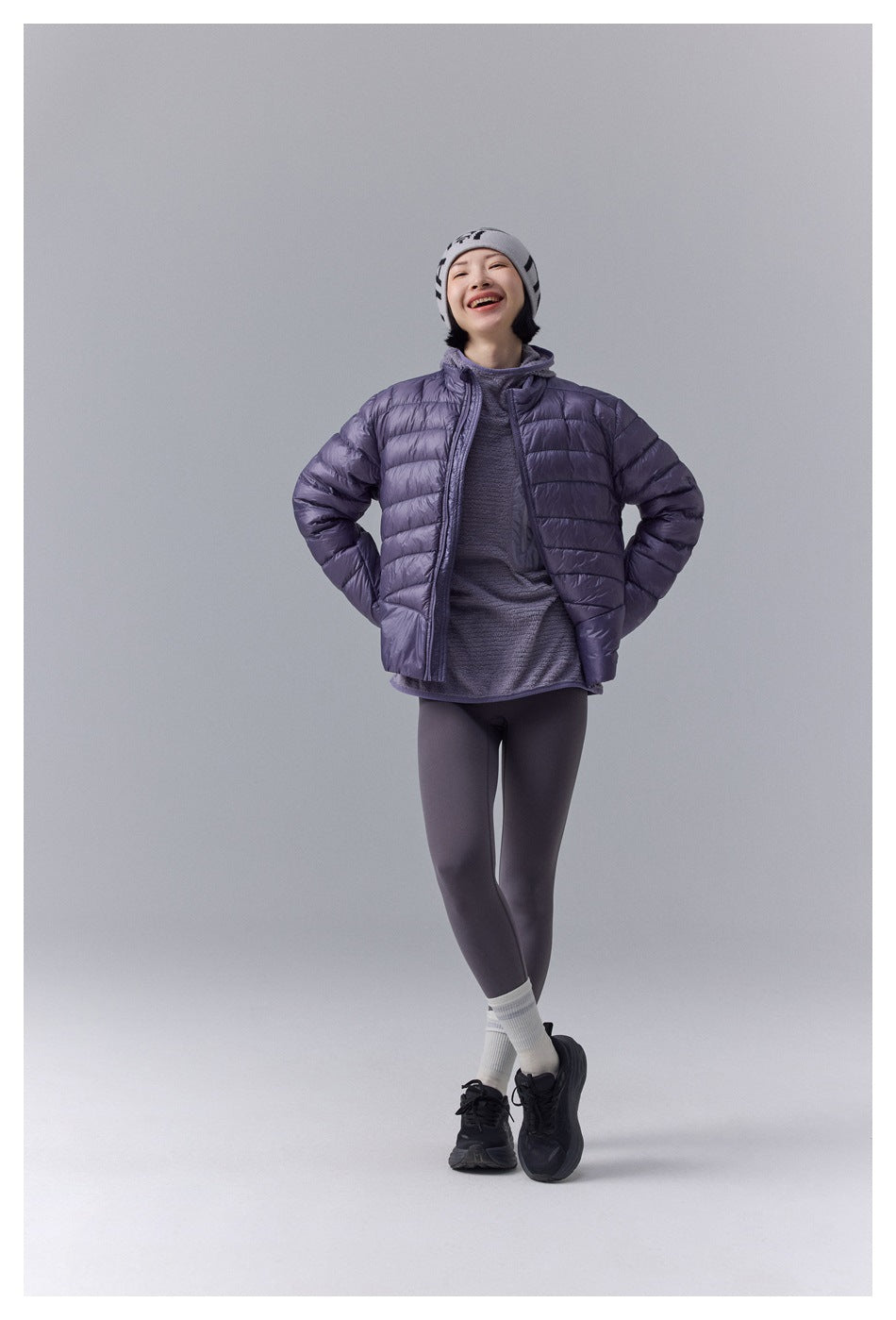 Smiling model wearing a purple quilted jacket over a matching top and dark leggings.