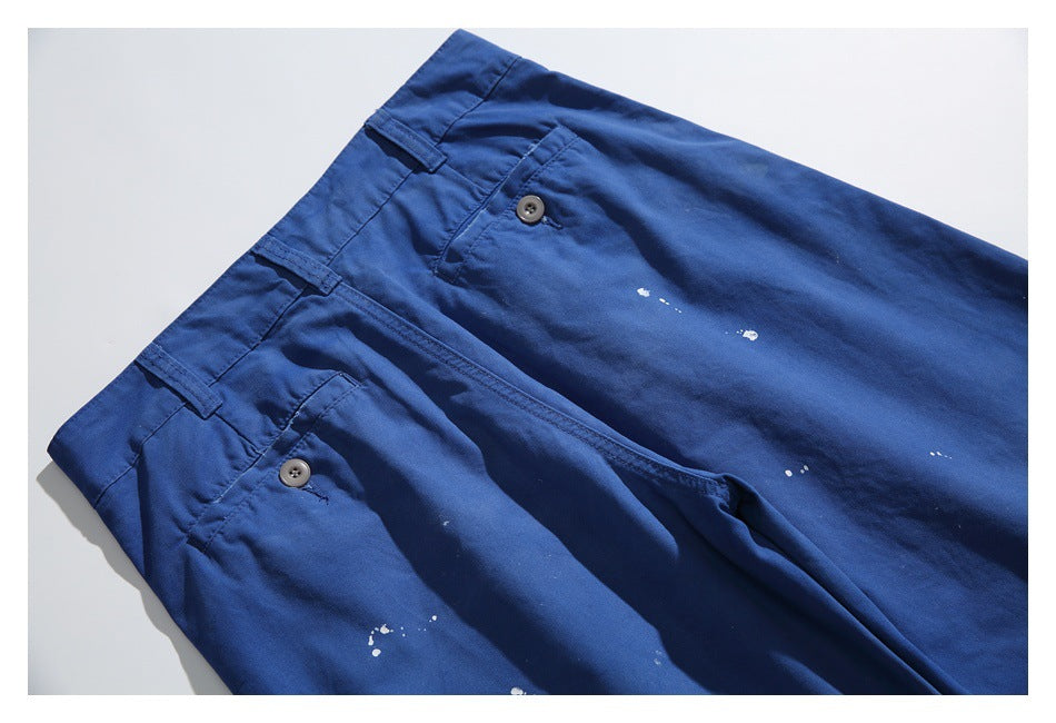 Angled close-up of royal-blue trousers showing the waistband, buttoned pockets, fly, and small white marks.