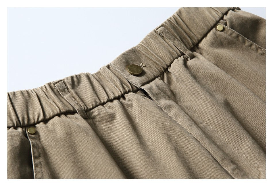 Close-up of taupe trousers showing a gathered elastic waistband and metal snaps.