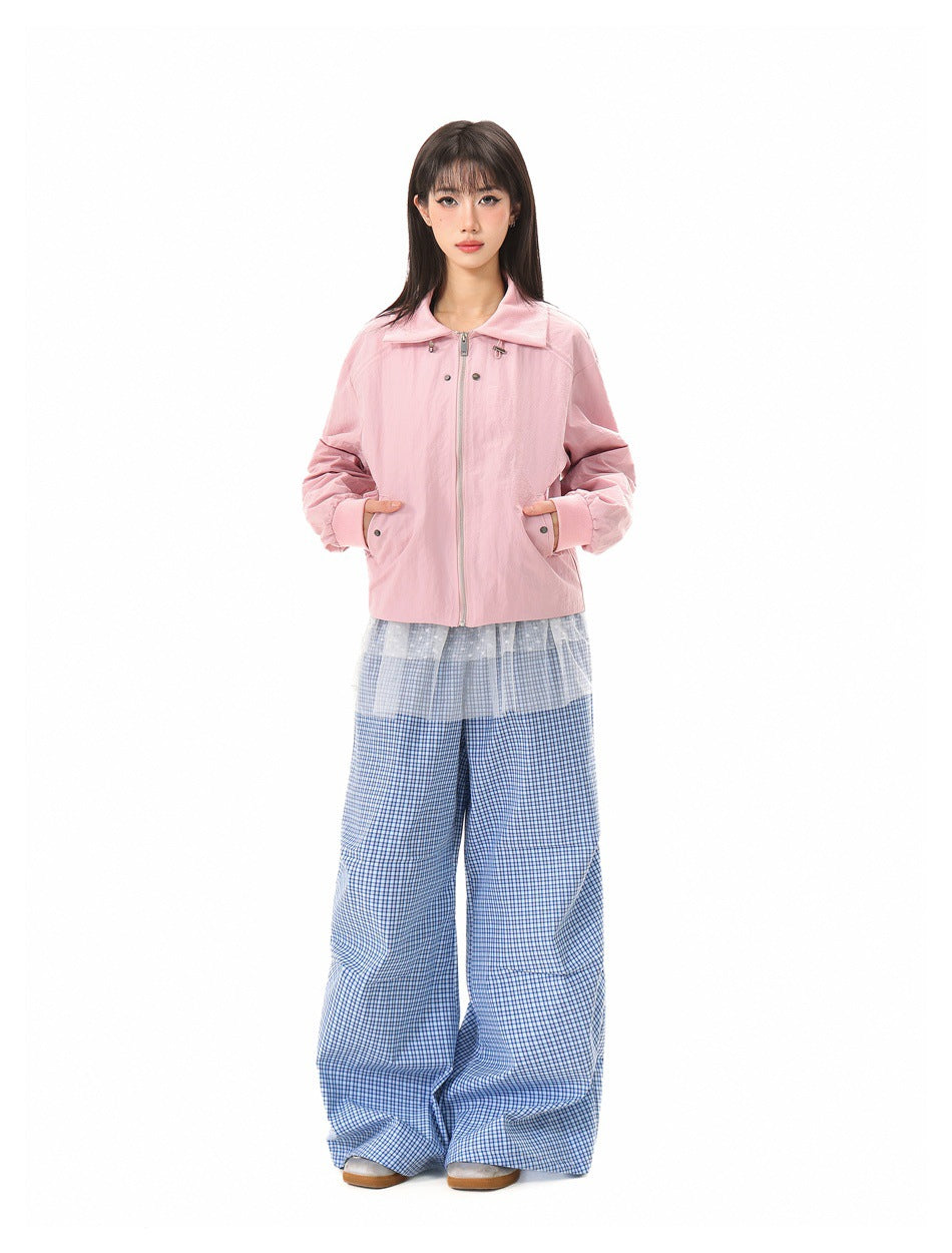 Full-length model wearing a light pink zip-front jacket with blue checkered wide-leg trousers.
