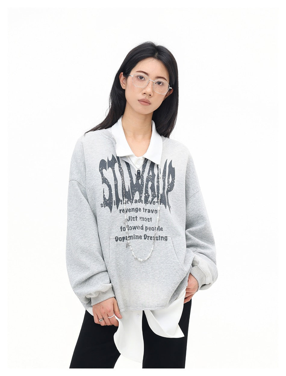 Woman in a gray oversized graphic sweatshirt layered over a white shirt, angled front view with a beaded necklace