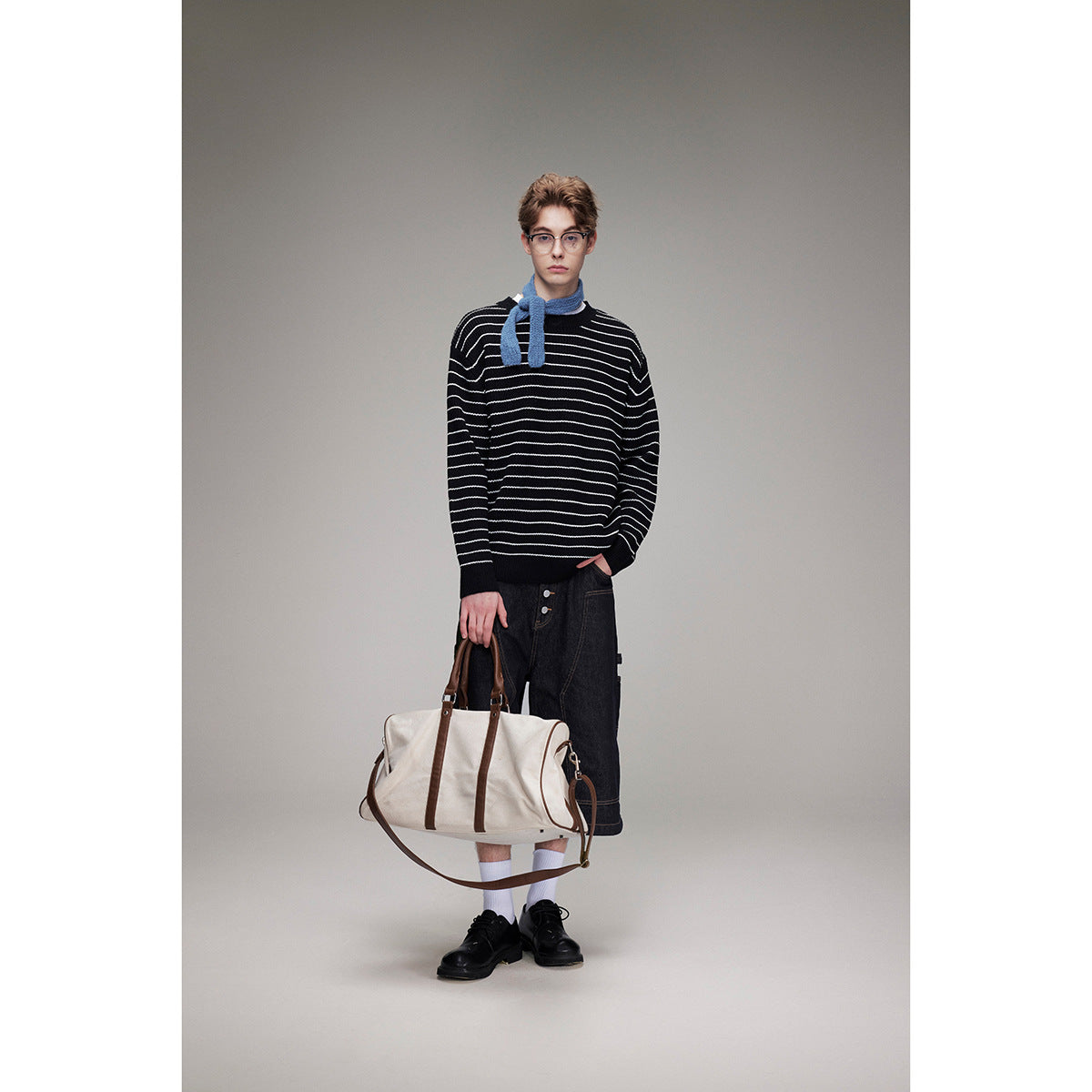 Model wearing a black sweater with thin white horizontal stripes, dark shorts, and a blue scarf.