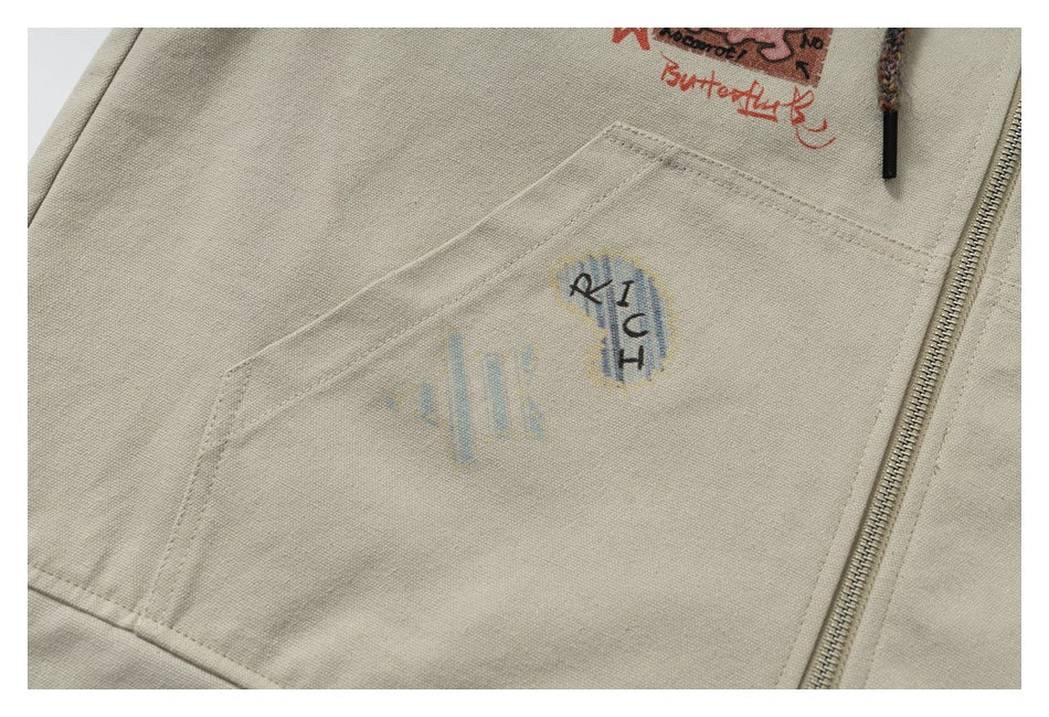 Close-up of a beige hoodie pocket with a small faded graphic and zipper alongside.