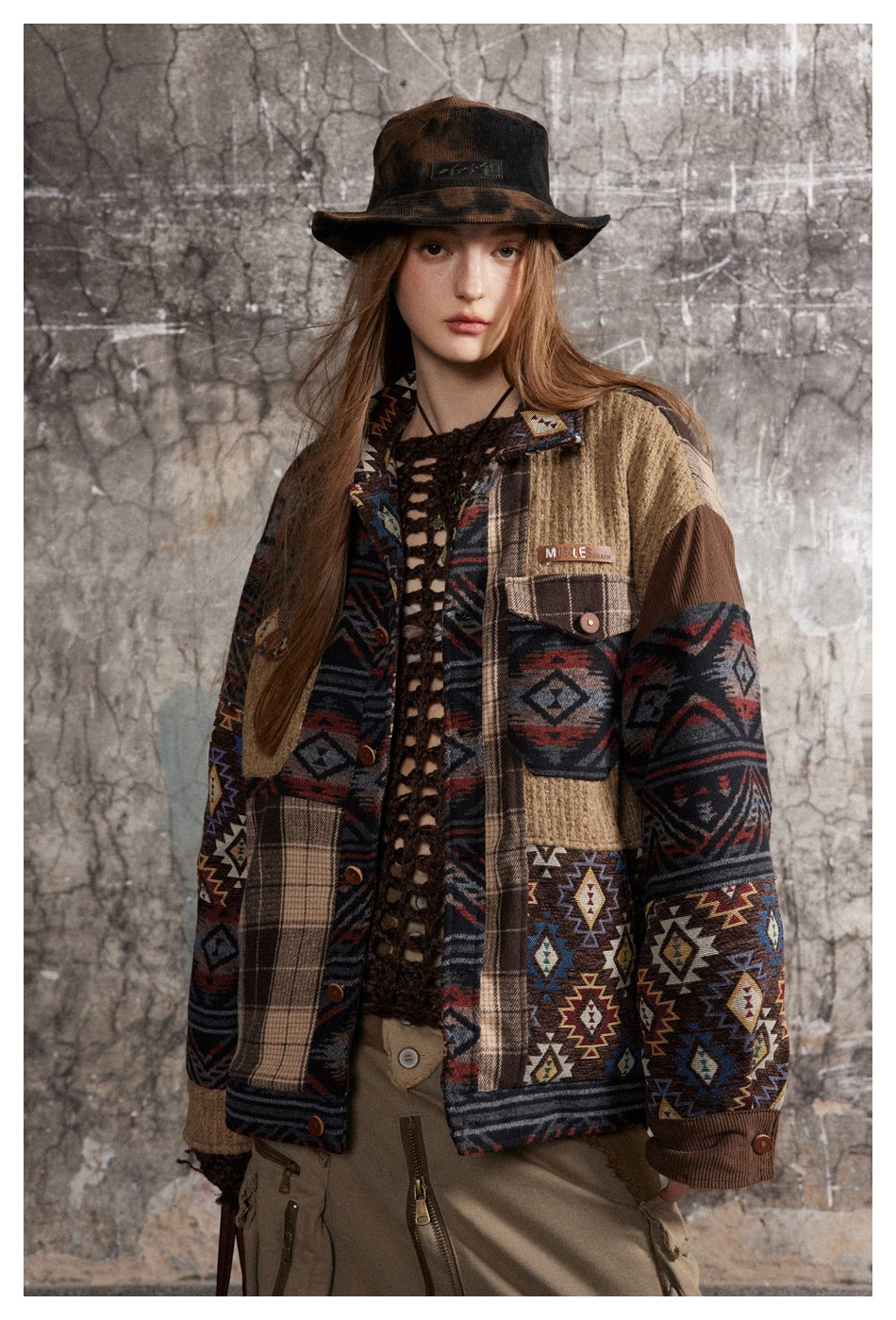 Front view of a model in a multicolored patchwork jacket with geometric, plaid, and ribbed tan panels.