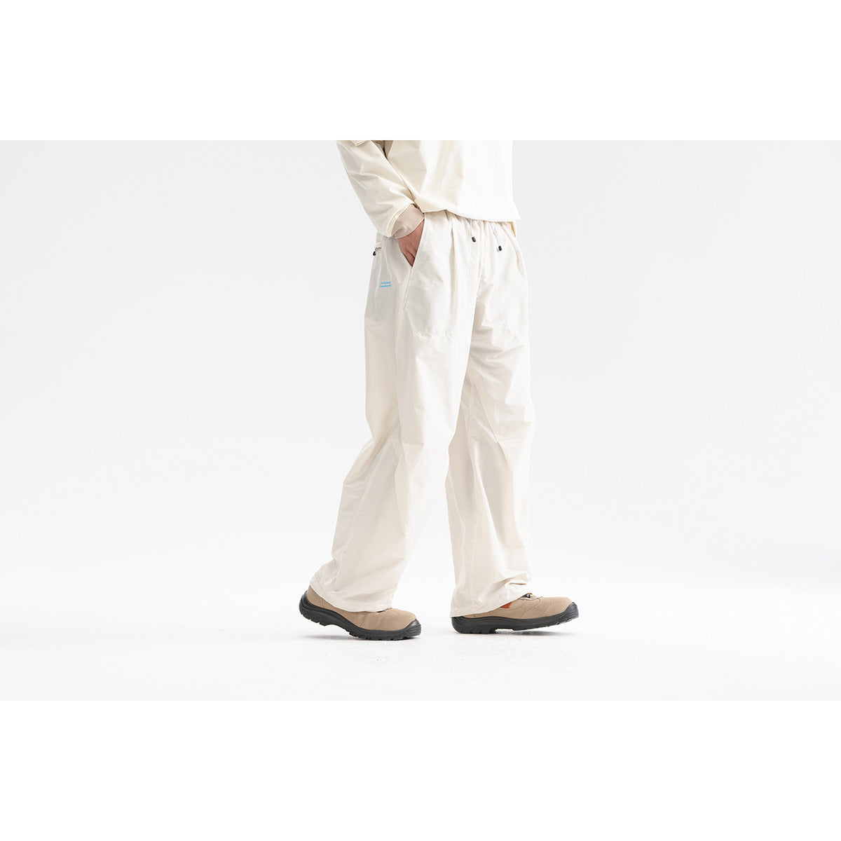 Cropped side view of a model wearing loose off-white trousers with an elastic waist and tan shoes.