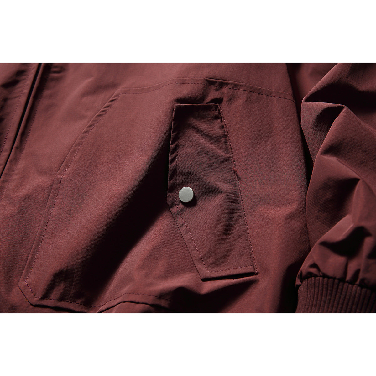 Close-up of the burgundy jacket’s flap hand pocket, silver snap, stitching and ribbed cuff.