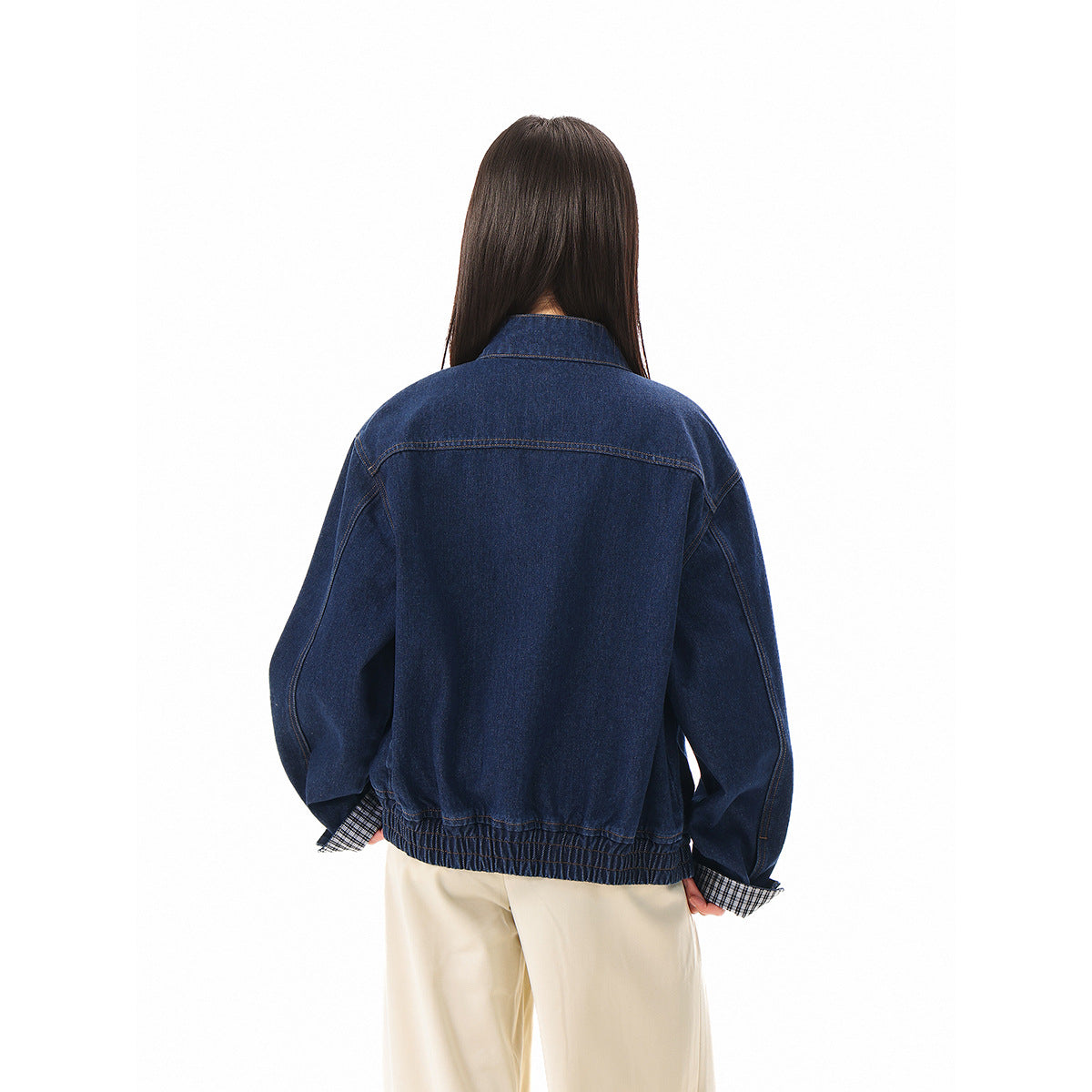 Rear view of a model wearing a dark blue denim jacket with a gathered hem and checked cuffs.