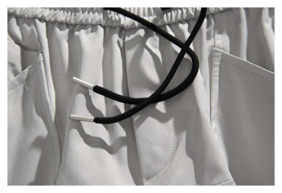 Close-up of black drawstrings with silver-colored tips over the front of light gray shorts.