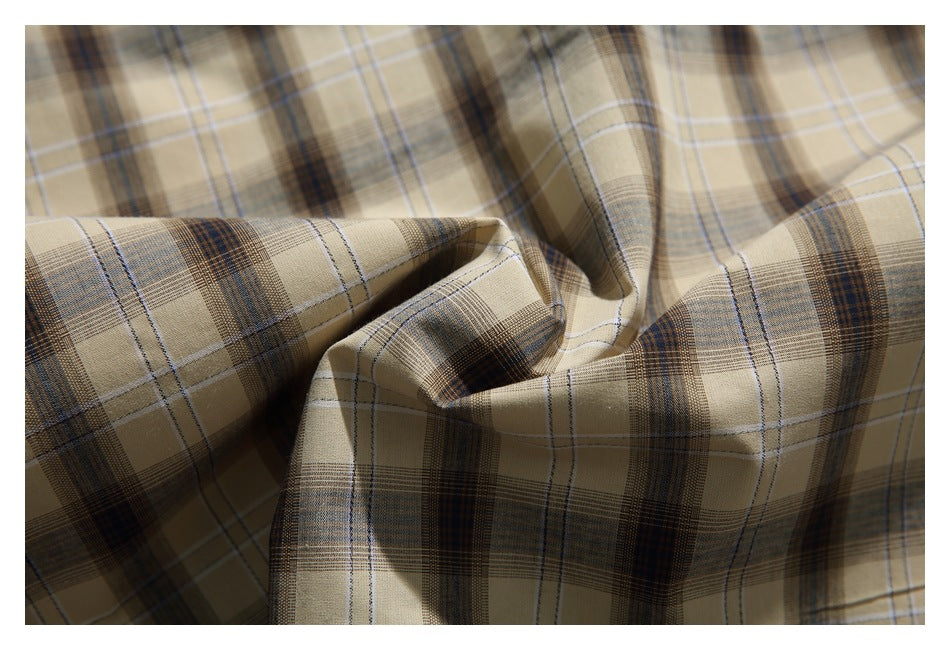 Close-up of beige fabric with brown and blue plaid lines, gathered to show its drape.