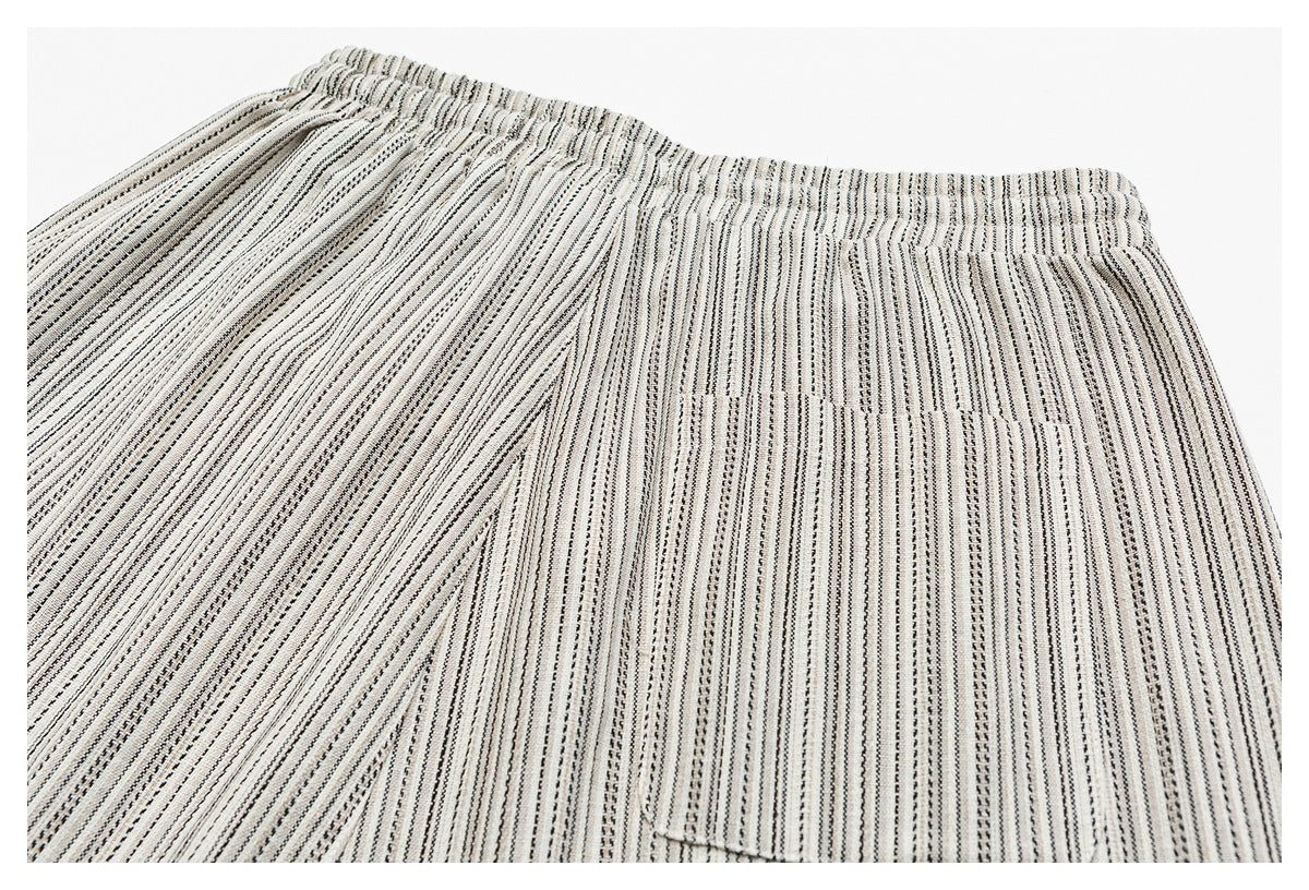 Flat lay of cream bottoms with narrow black and gray vertical stripes, an elastic waistband, and a front pocket.