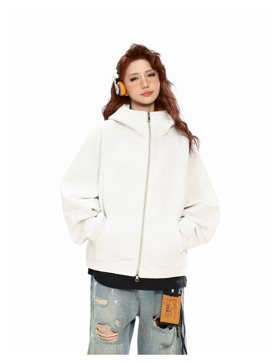 Model wearing a light gray oversized zip hoodie fully zipped, with hands in the pockets and distressed jeans.