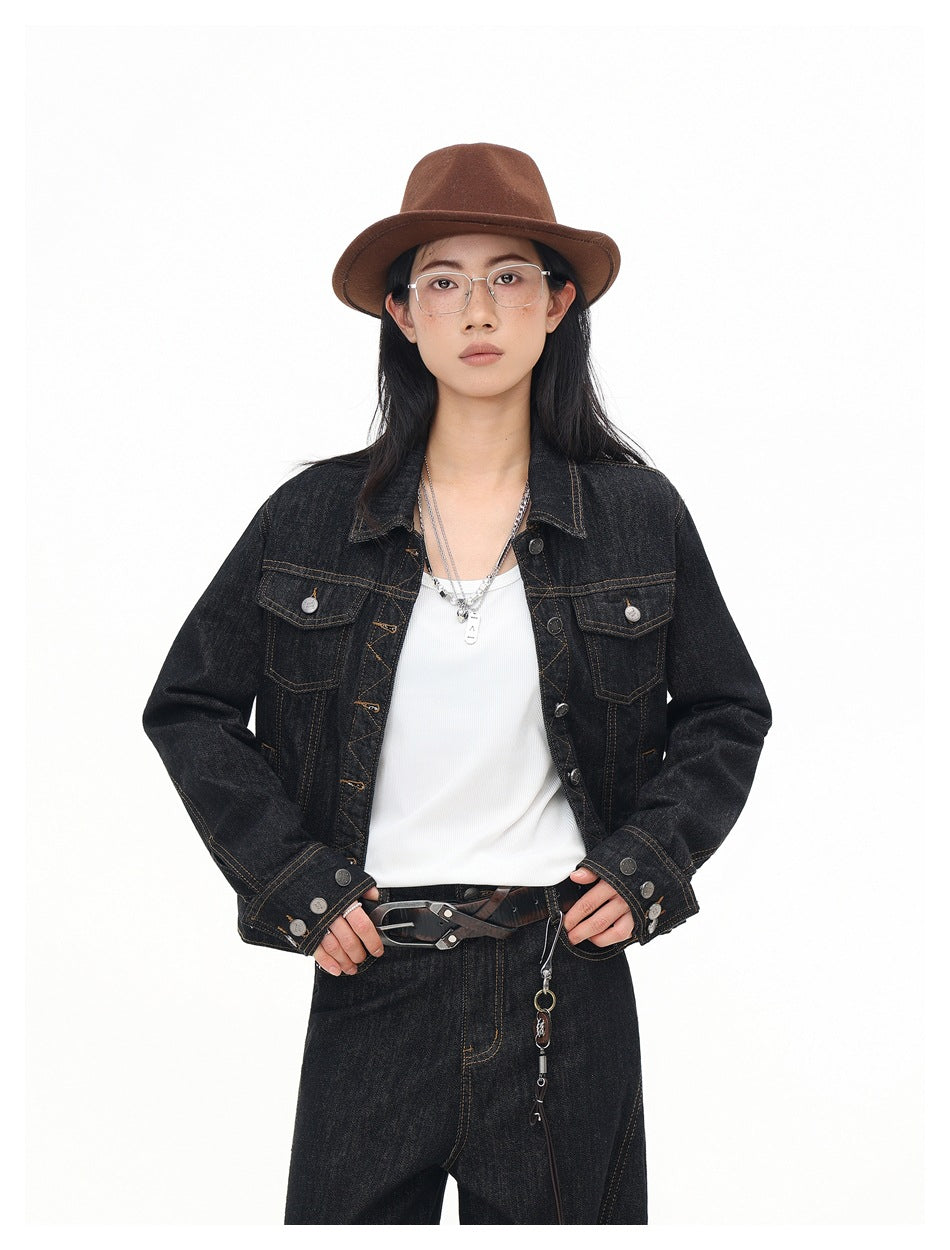 Front view of a model in a black denim jacket with metal buttons, flap pockets and contrast stitching.