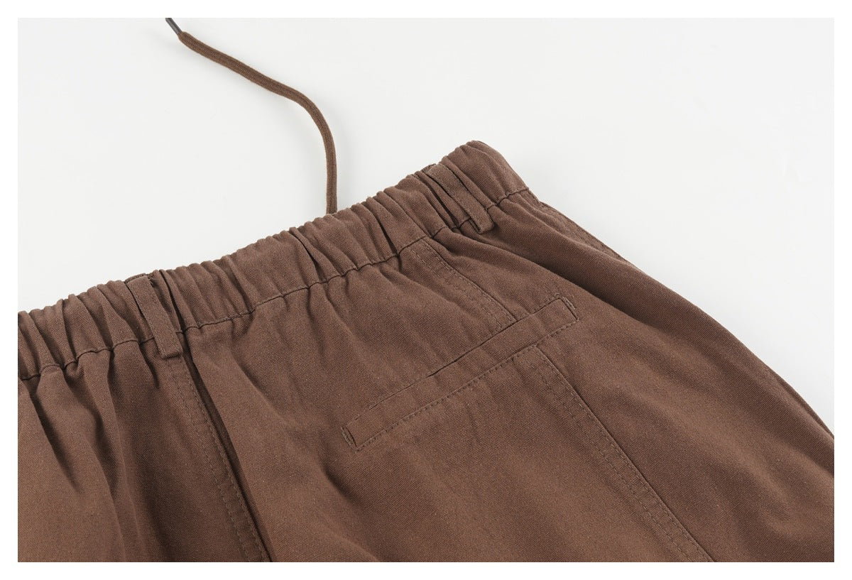Close-up of brown trousers showing the elastic waistband, drawstring, and rear pocket.