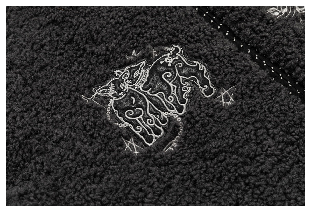 Close-up of an ornate light-colored embroidered motif on charcoal nubby fabric.