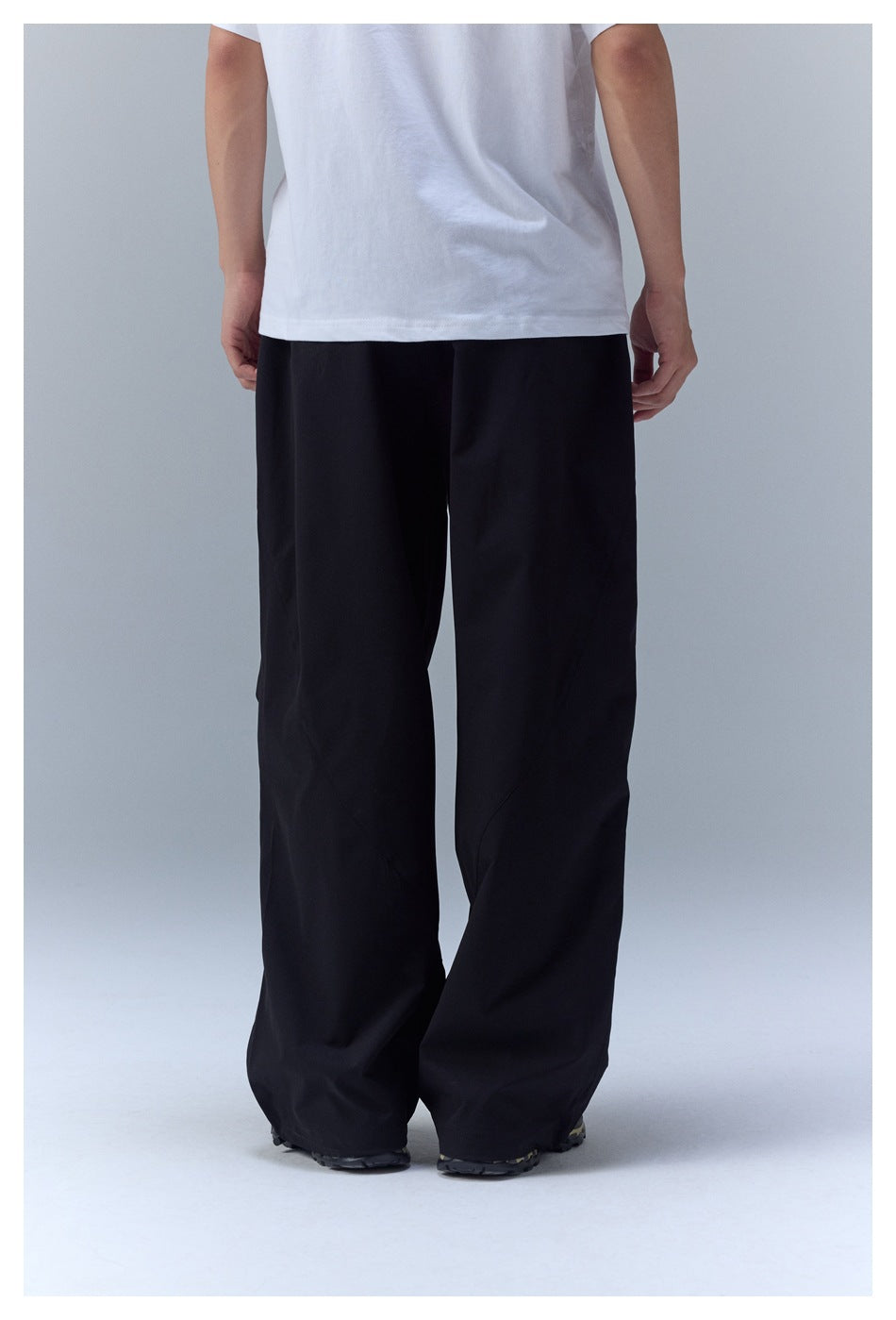 Back view of a person wearing loose black pants with a white T-shirt and trail shoes.