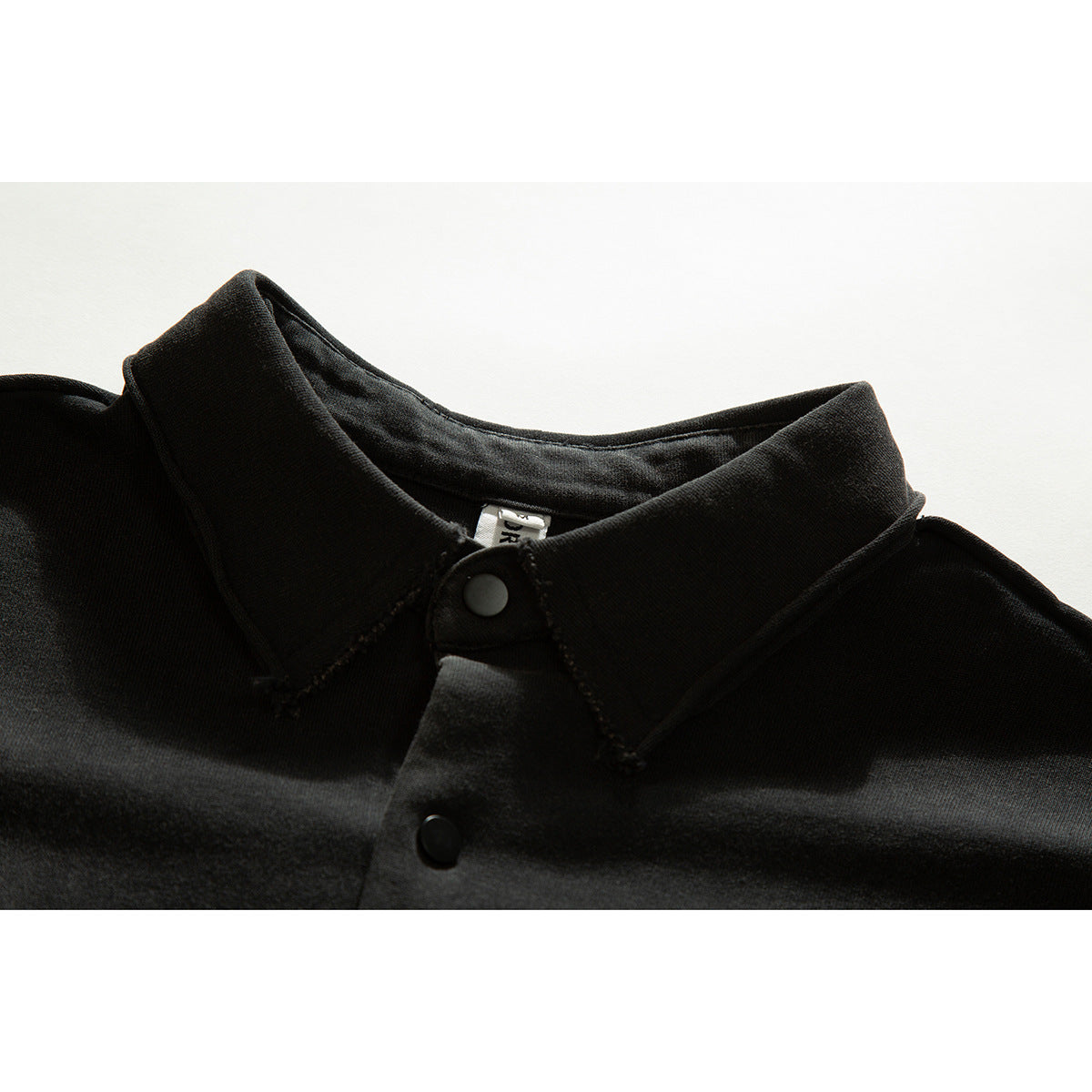 Close-up of a black shirt collar with a snap button and a partially visible inner label.