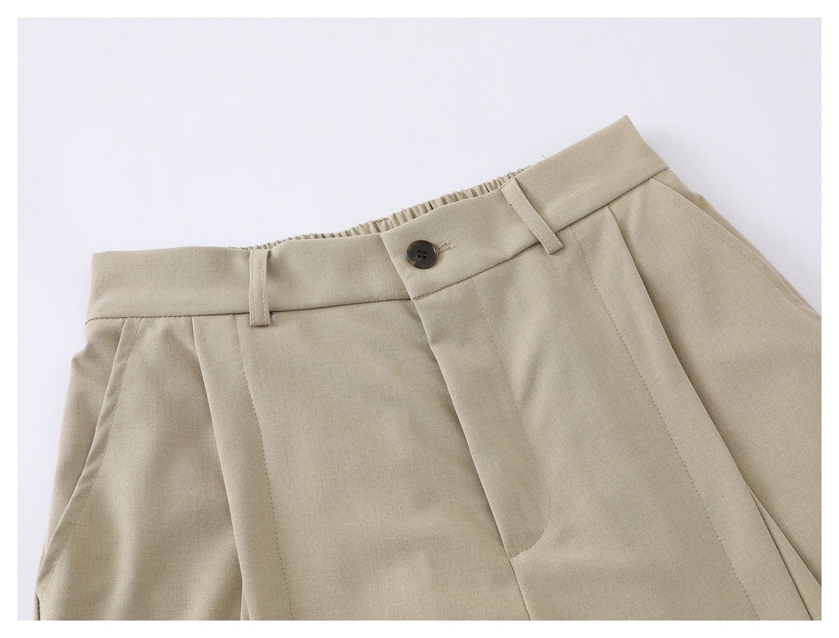 Close-up of beige shorts showing the buttoned waistband, belt loops, pleats and front fly.